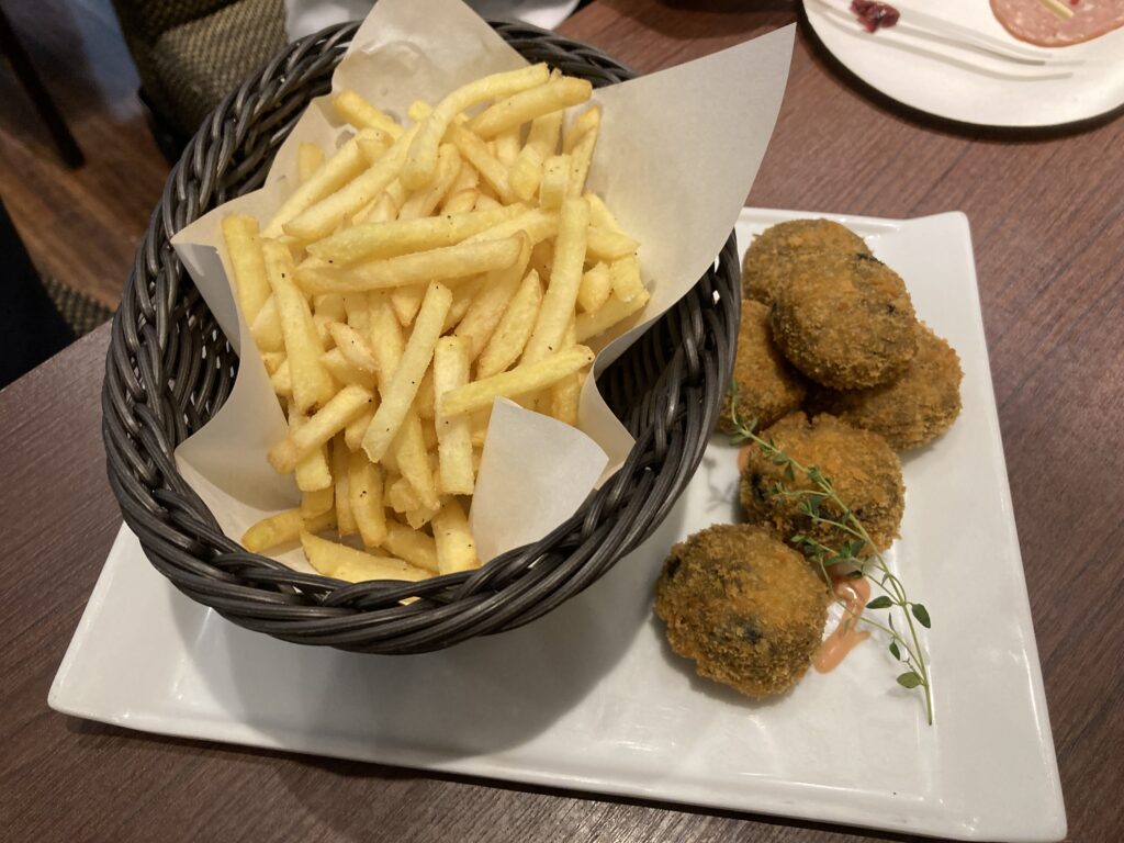 四角い白皿の上に、トリュフ風味のフライドポテトのバスケットと、小さなライスコロッケ